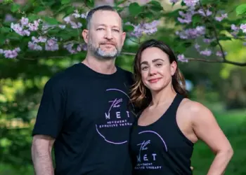 Two adults in black The MET shirts posing outdoors under flowering pink blossoms, smiling at the camera.
