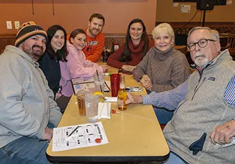 Group of eight adults sitting around a restaurant table, smiling, with menus and drinks on the table.