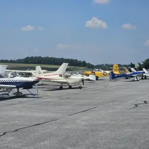 Line of small propeller airplanes parked in a row on a sunny airport tarmac under a blue sky