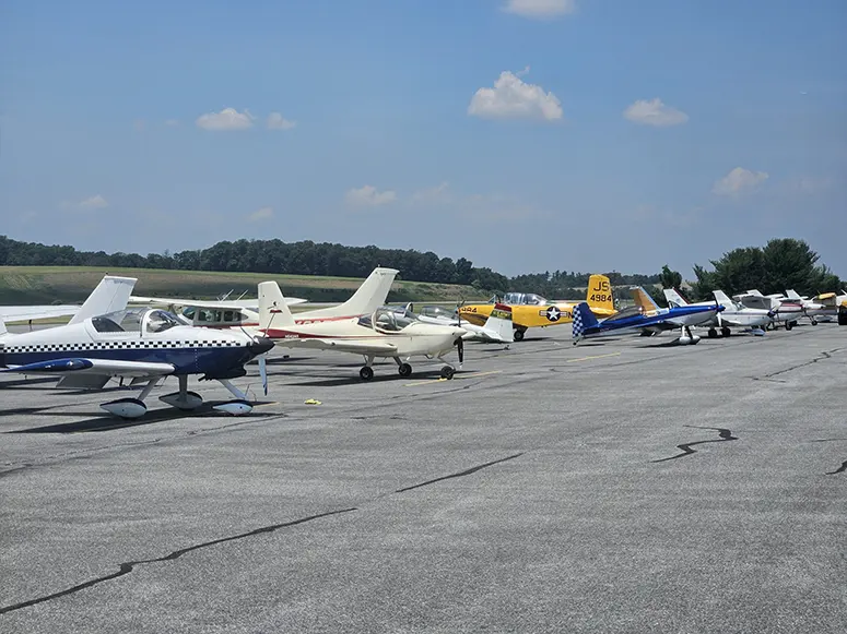 Line of small propeller airplanes parked in a row on a sunny airport tarmac under a blue sky