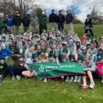 Large group of students and instructors posing on a grassy hill, holding a green First Green banner.