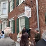 Crowd of people gathered outside a brick building with a hanging sign reading 'Cockey's Library of Carroll County History' outside the Historical Society.