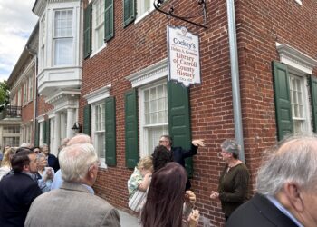 Crowd of people gathered outside a brick building with a hanging sign reading 'Cockey's Library of Carroll County History' outside the Historical Society.
