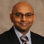 Professional head-and-shoulders portrait of a smiling man wearing glasses, a suit, and striped tie.