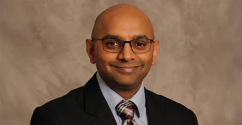Professional head-and-shoulders portrait of a smiling man wearing glasses, a suit, and striped tie.