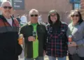 Four adults standing together outdoors at a community event, each holding a drink and smiling.