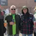 Four adults standing together outdoors at a community event, each holding a drink and smiling.