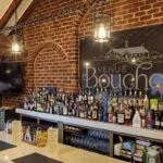 Brick-walled bar with wooden beams, a long white counter filled with assorted liquor bottles and a large Venue Bouchon sign on the brick wall behind.