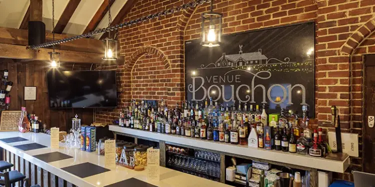 Brick-walled bar with wooden beams, a long white counter filled with assorted liquor bottles and a large Venue Bouchon sign on the brick wall behind.