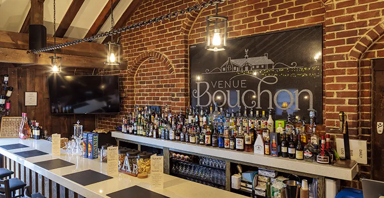 Brick-walled bar with wooden beams, a long white counter filled with assorted liquor bottles and a large Venue Bouchon sign on the brick wall behind.
