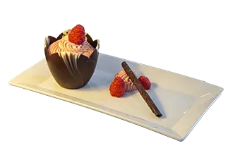 Chocolate cup dessert with cream and raspberries on a white rectangular plate with a chocolate stick.