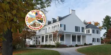 Large white historic house with a wraparound porch on a curved driveway, autumn trees, and an overlaid circular US 250 commemorative seal.