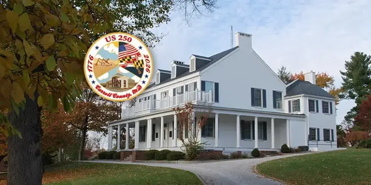 Large white historic house with a wraparound porch on a curved driveway, autumn trees, and an overlaid circular US 250 commemorative seal.
