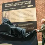 Two people unveil a plaque for the McDaniel College Kahler Nursing Education Center against a brick wall outside a hospital setting.