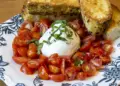 Plate of chopped cherry tomatoes around a burrata ball, topped with basil, with toasted bread slices on a blue-and-white patterned plate.