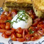 Burrata Pomodoro_1 - Carroll News | Carroll Publications | Carroll County, MD Plate of chopped cherry tomatoes around a burrata ball, topped with basil, with toasted bread slices on a blue-and-white patterned plate.