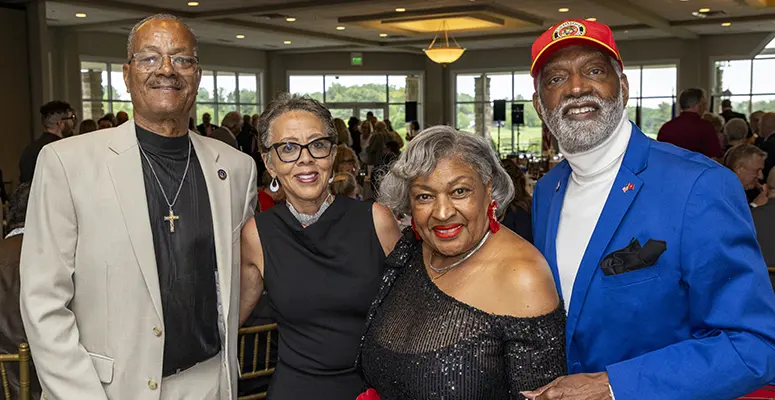 Four adults in formal attire posing for a group photo at a banquet hall.