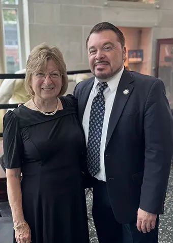 tom-gordon-iii-graduation - Carroll News | Carroll Publications | Carroll County, MD Two smiling adults pose together indoors, the woman in a black dress and the man in a dark suit and patterned tie.